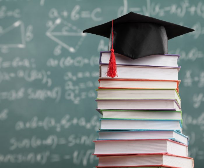 Stock image of a stack of colorful text books with a graduation cap on top